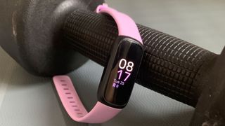 Die Fitbit Inspire 3 in rosa, über eine Hantel gelegt