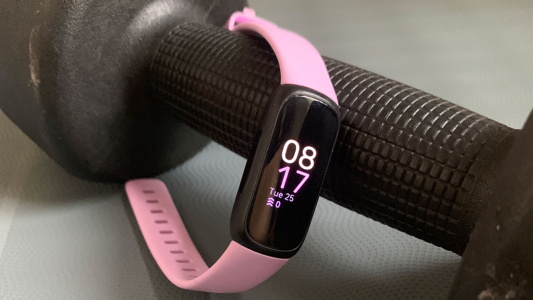 The Fitbit Inspire 3 in pink attached to a small dumbbell.