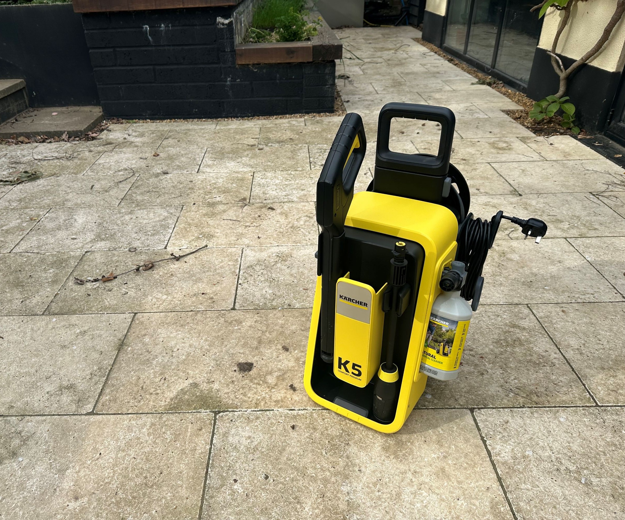 A yellow K&amp;auml;rcher K5 Comfort Premium pressure washer on a cream limestone patio