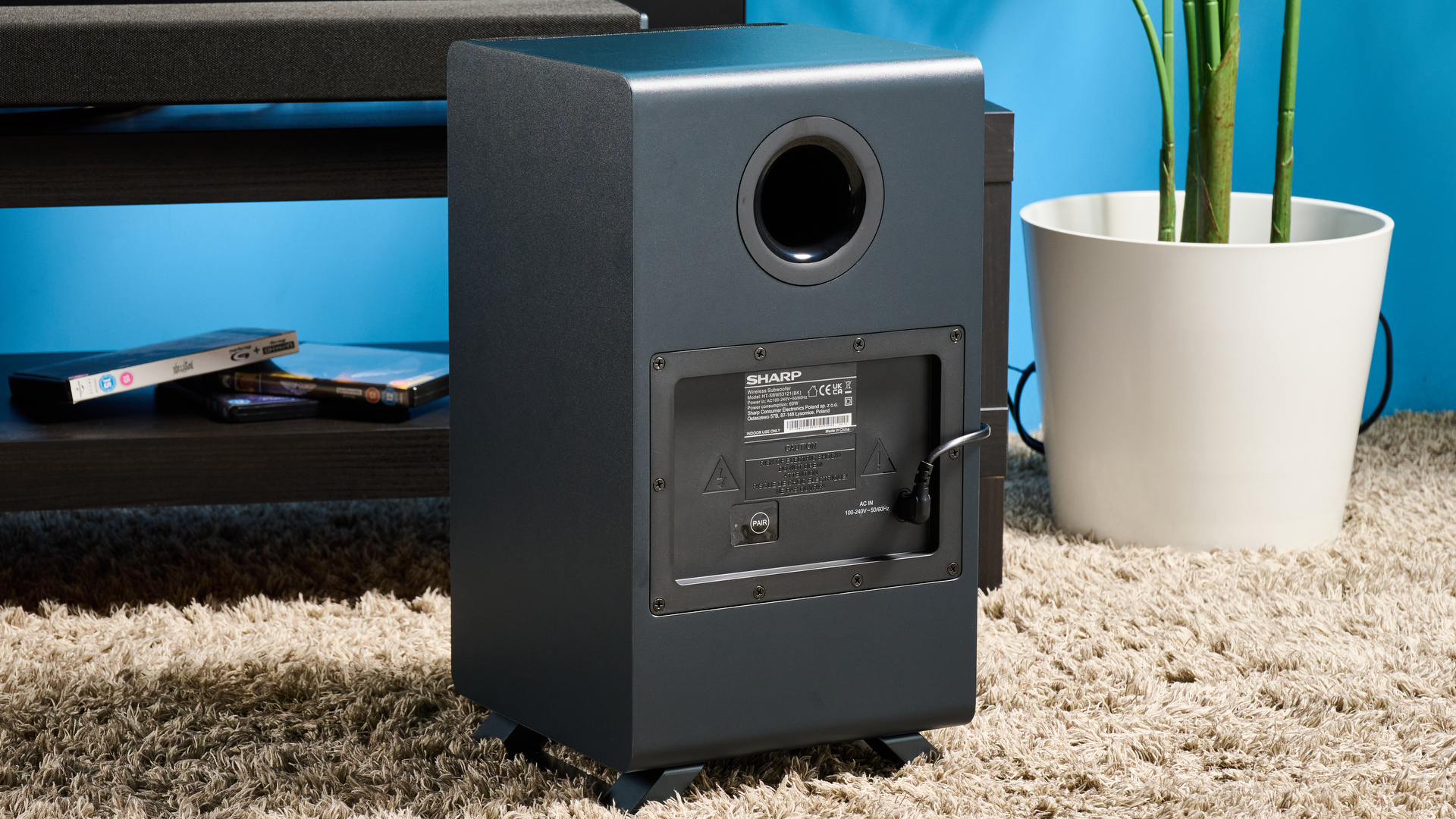 the Sharp 3.1.2 HT-SBW53121 Soundbar in black with a remote, subwoofer, against a blue background next to a panasonic TV
