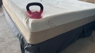 A weight balances on the corner of the Saatva Contour5 Mattress, demonstrating a lot of sink and poor edge support