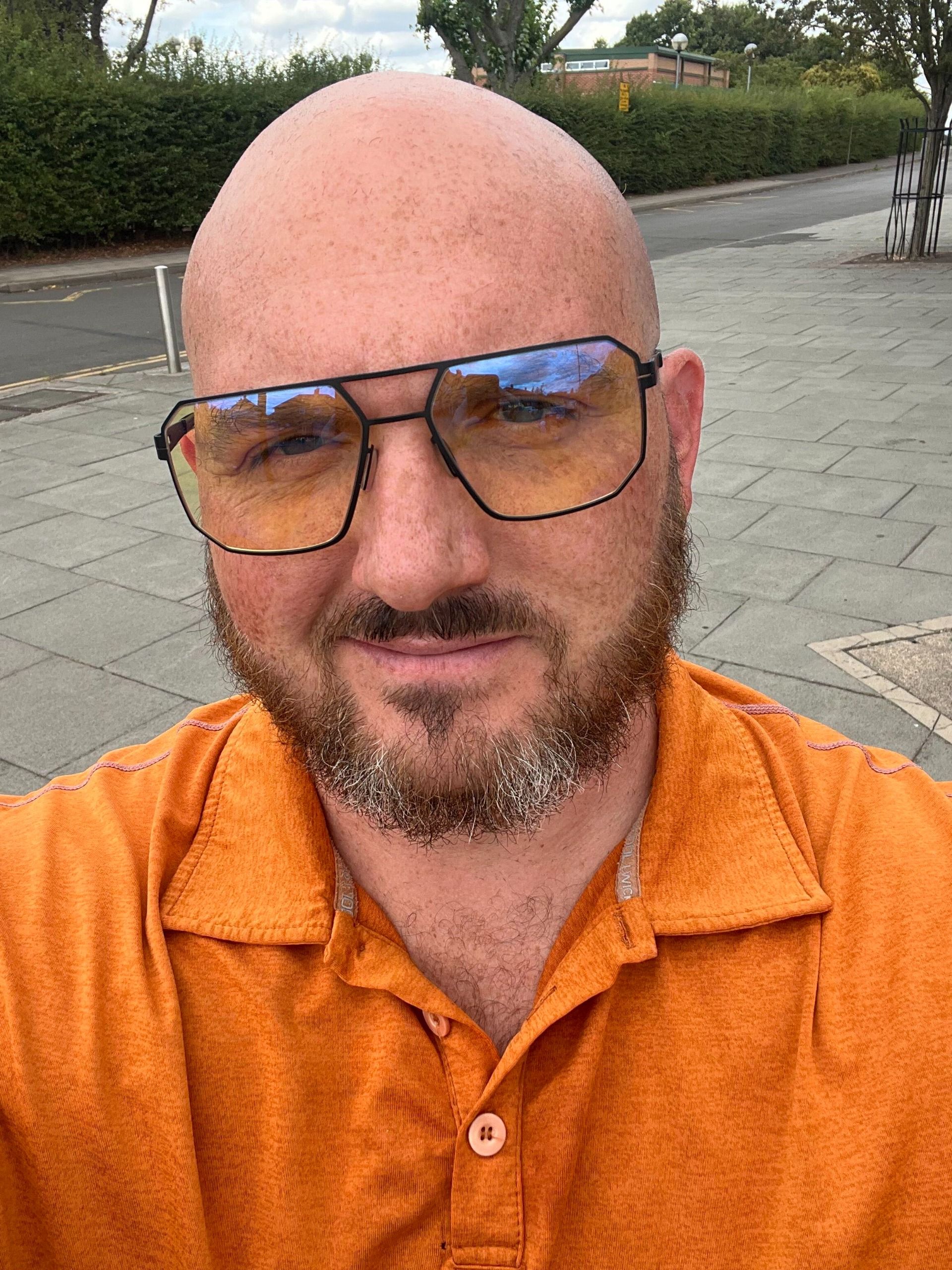 Close-up selfie of a person wearing amber-tinted Gunnar glasses outdoors on a paved sidewalk.