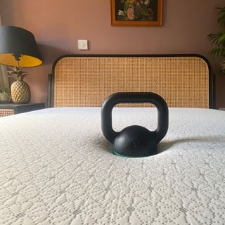 A kettlebell resting on a mattress in a bedroom with salmon pink walls