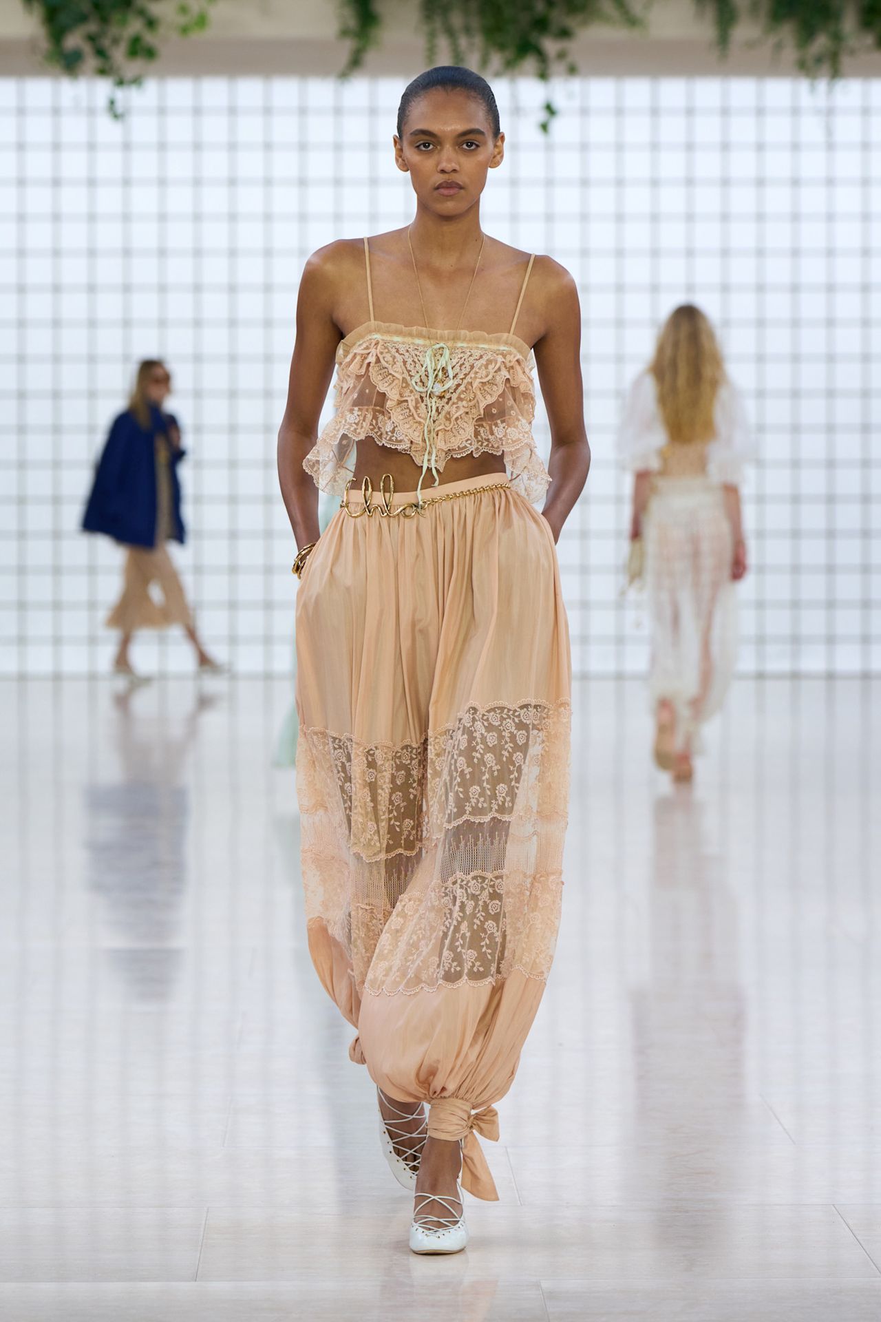A model wearing a sheer lace top and matching genie pants on the runway at Chlo&eacute;'s spring/summer 2025 show.