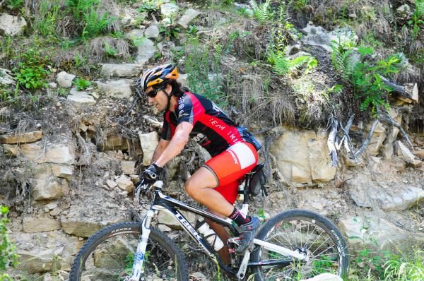 A rider traverses some off-camber singletrack next to a sketchy rock wall.