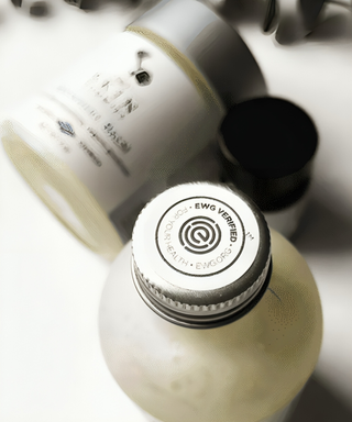 A product bottle with a metal screw cap, the EWG safety mark stamped on the lid