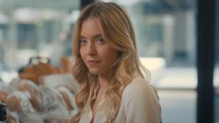 Sydney Sweeney standing in a coffee shop almost smiling in Anyone But You. She will be starring in The Housemaid.