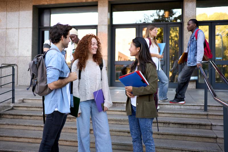 Three students talking by steps leading to their university campus