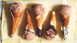 Five chocolate and Baileys ice creams in homemade cones laid out on a yellow piece of cloth