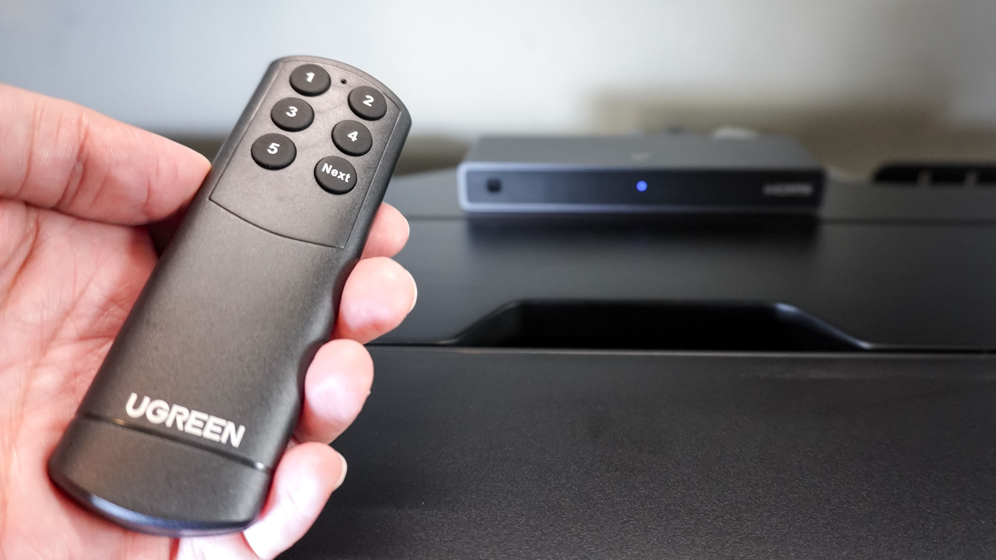 The Ugreen 8K@60Hz HDMI Switch with the included controller in hand at the very back of the Corsair Platform:4 Elevate Desk