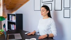 Woman sits at a desk with her hands on the desk and her eyes closed.