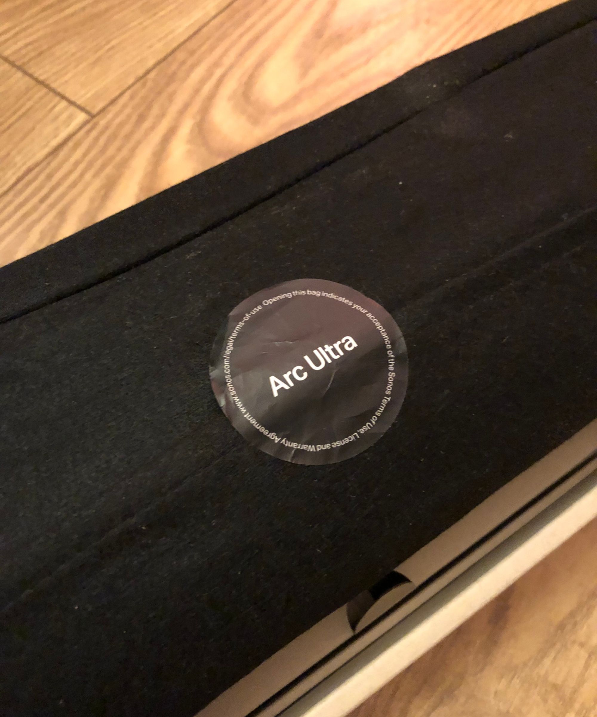 Sonos Arc Ultra in soft, protective sleeve, still in box, on wooden floor in Dan Fauzi's home.