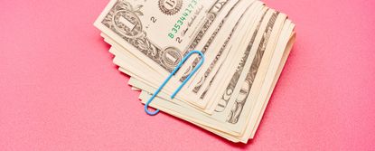 Directly above shot of a bundle of American Dollar bank notes with blue paper clip on pink background