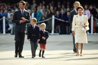 Young Prince William and Prince Harry wear suits and walk alongside Prince Charles and Princess Margaret, who wears a lemon skirt suit