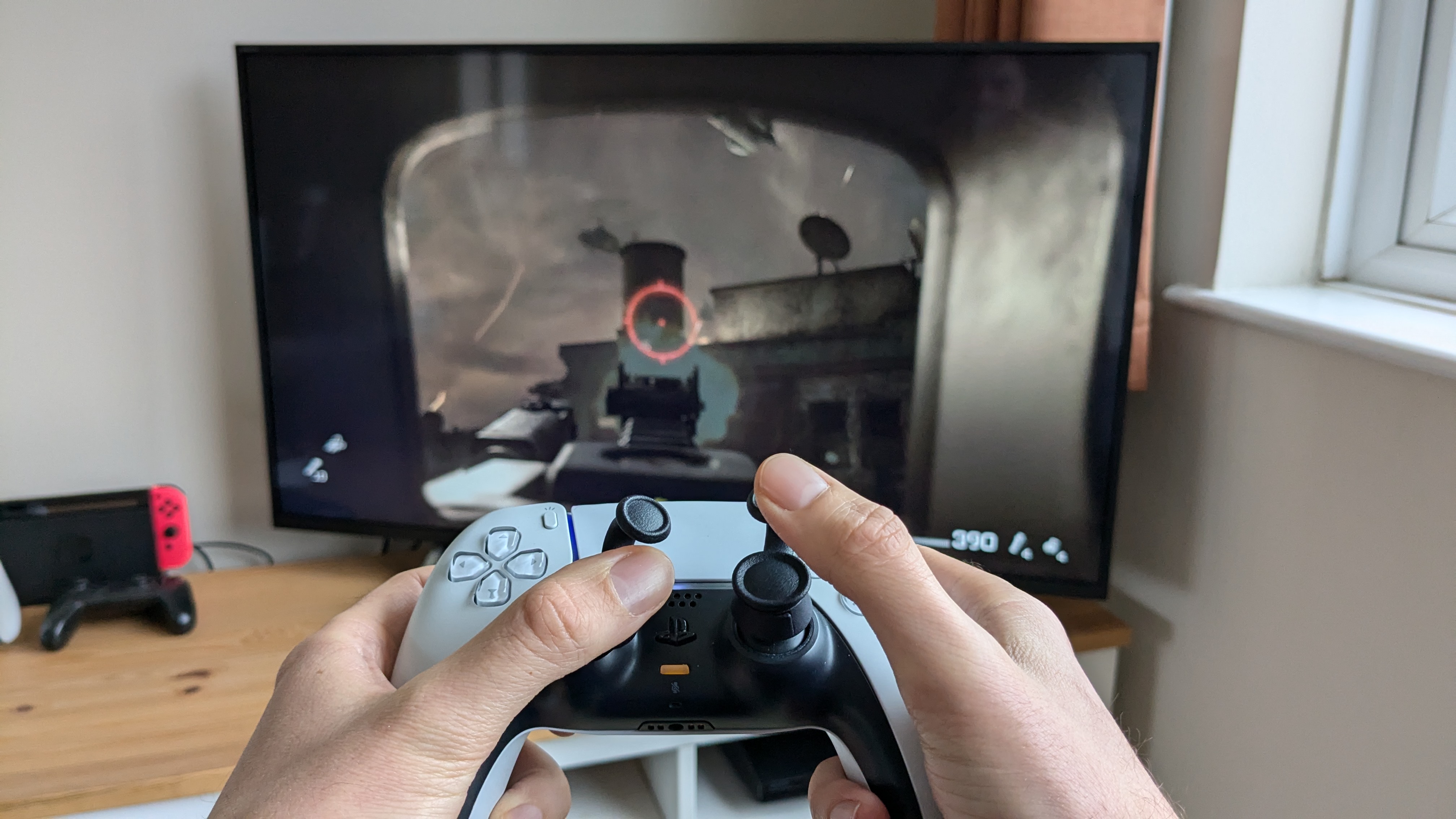 A DualSense Wireless Controller in the hands of an adult with two Thumb Soldier attachments on each stick.