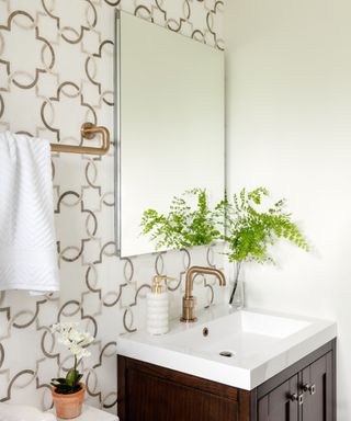 A bathroom with a white and gold patterned wall, a shallow mirror medicine cabinet, and white and brown sink
