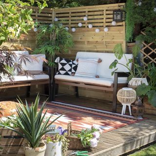 raised deck in corner of garden with two garden sofas gardening screen garden rug and festoon lights