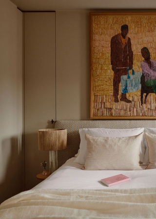 A bedroom with a side table and a lamp, and a large framed painting above the bed