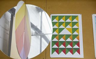 A round mirrored object next to a piece of paper with a colourful triangular pattern on it on a wooden table.