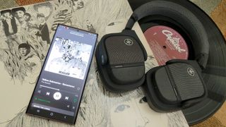 The Yamaha YH-L700A headphones on a vinyl copy of The Beatles' Revolver album. A phone next to the headphones is playing the same album from Spotify