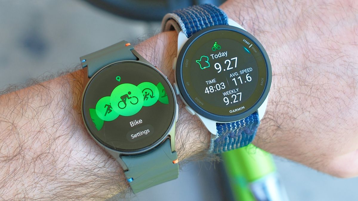 Close up of a Samsung Galaxy Watch 7 and Garmin Forerunner 165 on a user&#039;s wrist next to each other with a lime green bike in the background