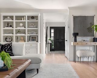 Light gray styled hutch in open plan space with light wooden floors, facing the front door with black kitchen visible on the right