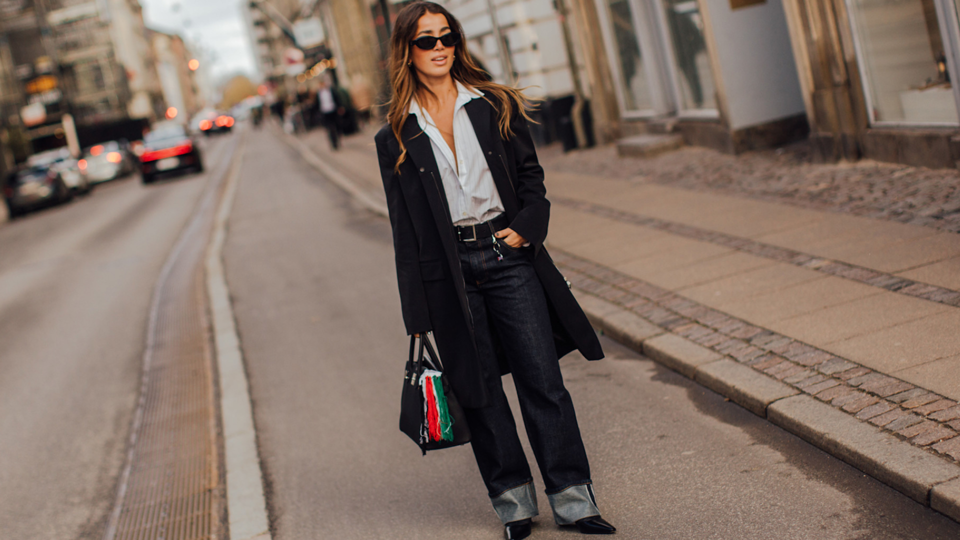 Fashion week attendee wearing sunglasses, button down shirt, black coat, cuffed jeans