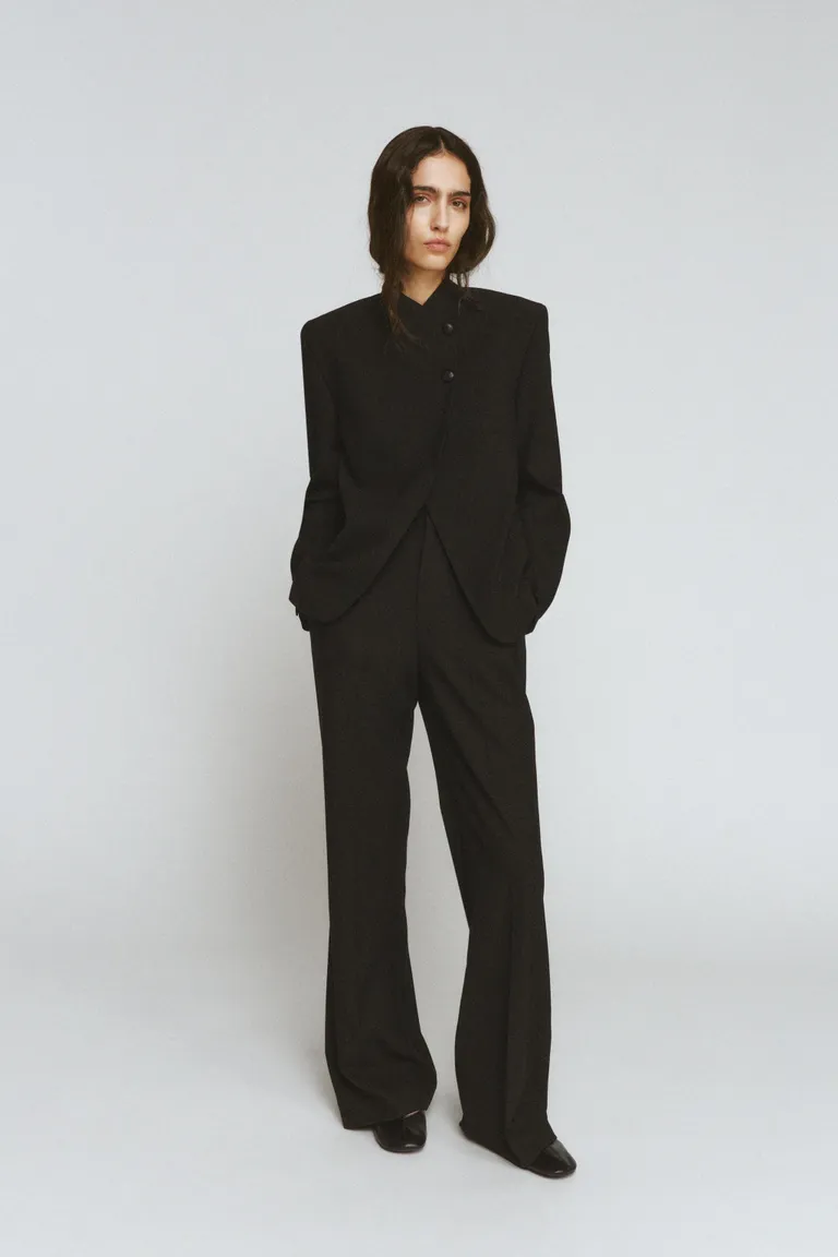 Woman wears high neck blazer and black tailored trousers