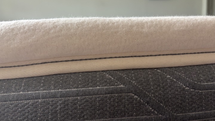 A close-up shot of the The Birch Plush Organic Mattress Topper's organic cotton cover on top of a memory foam bed.