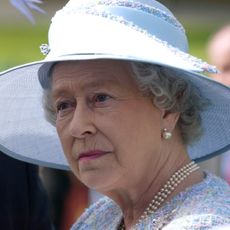 Queen Elizabeth wears a blue hat and a pearl necklace