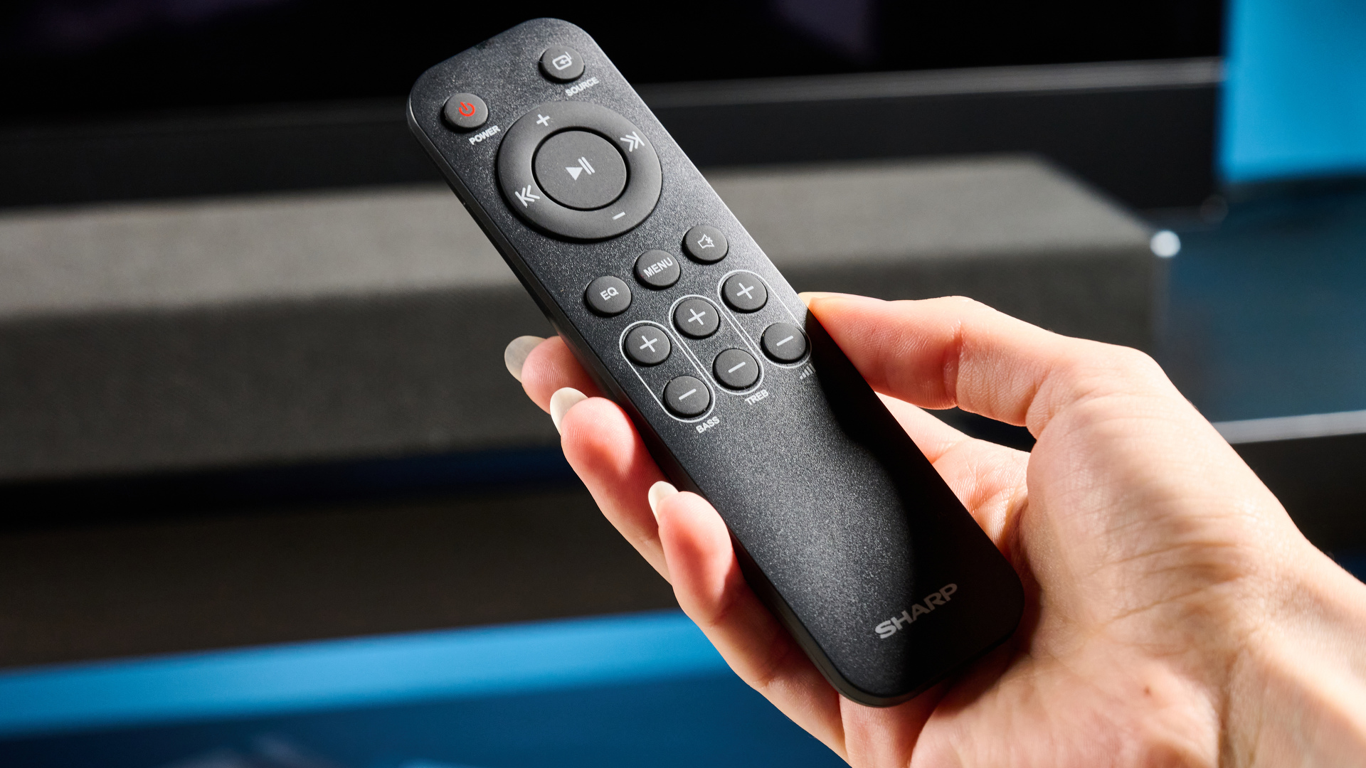the Sharp 3.1.2 HT-SBW53121 Soundbar in black with a remote, subwoofer, against a blue background next to a panasonic TV