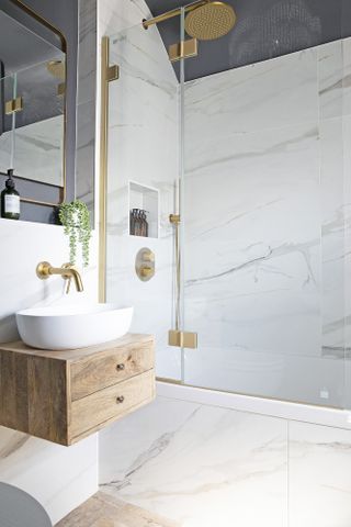 Small bathroom with large-format marble wall and floor tiles, gold hardware and wood-effect wall hanging basin unit