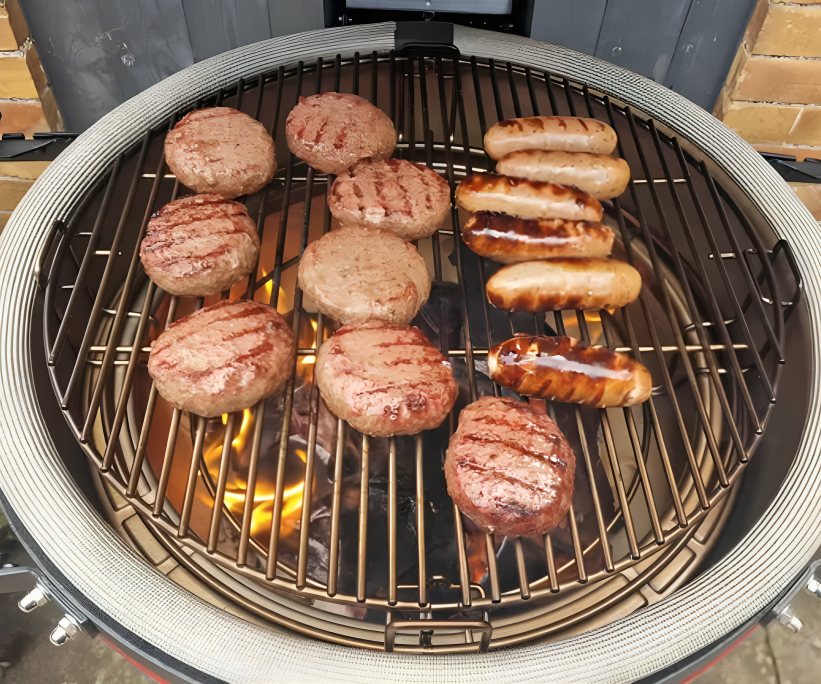 Kamado Joe Classic Joe II grill with cooking burgers and sausages on the griddle.