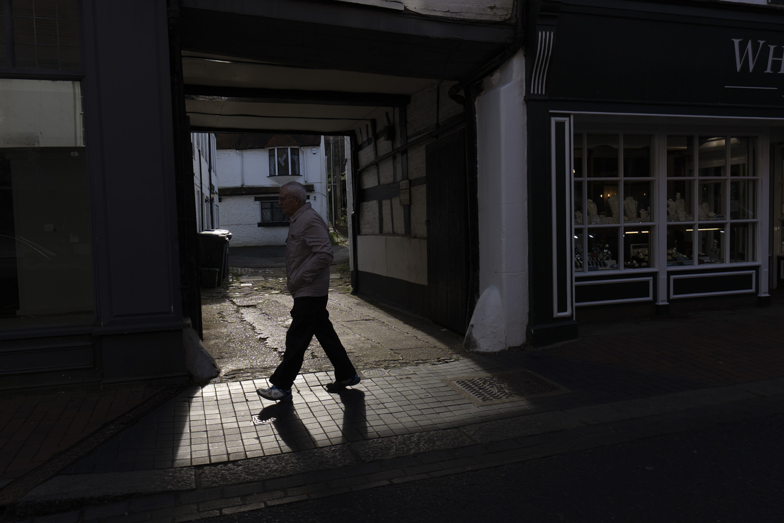 Picture taken with Panasonic S5 II of street scene decisive moment man walking into shaft of light