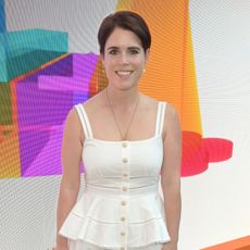 Princess Eugenie wearing a white dress standing in front of a colorful wall