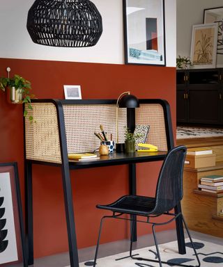 A home office with rusty red wall paint decor and wood/cane detail black office desk