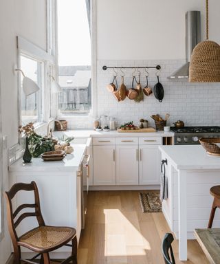 kitchen renovation rules, white kitchen with white cabinetry, white tiles, brass hanging rail with copper pans, rattan pendant, light and airy