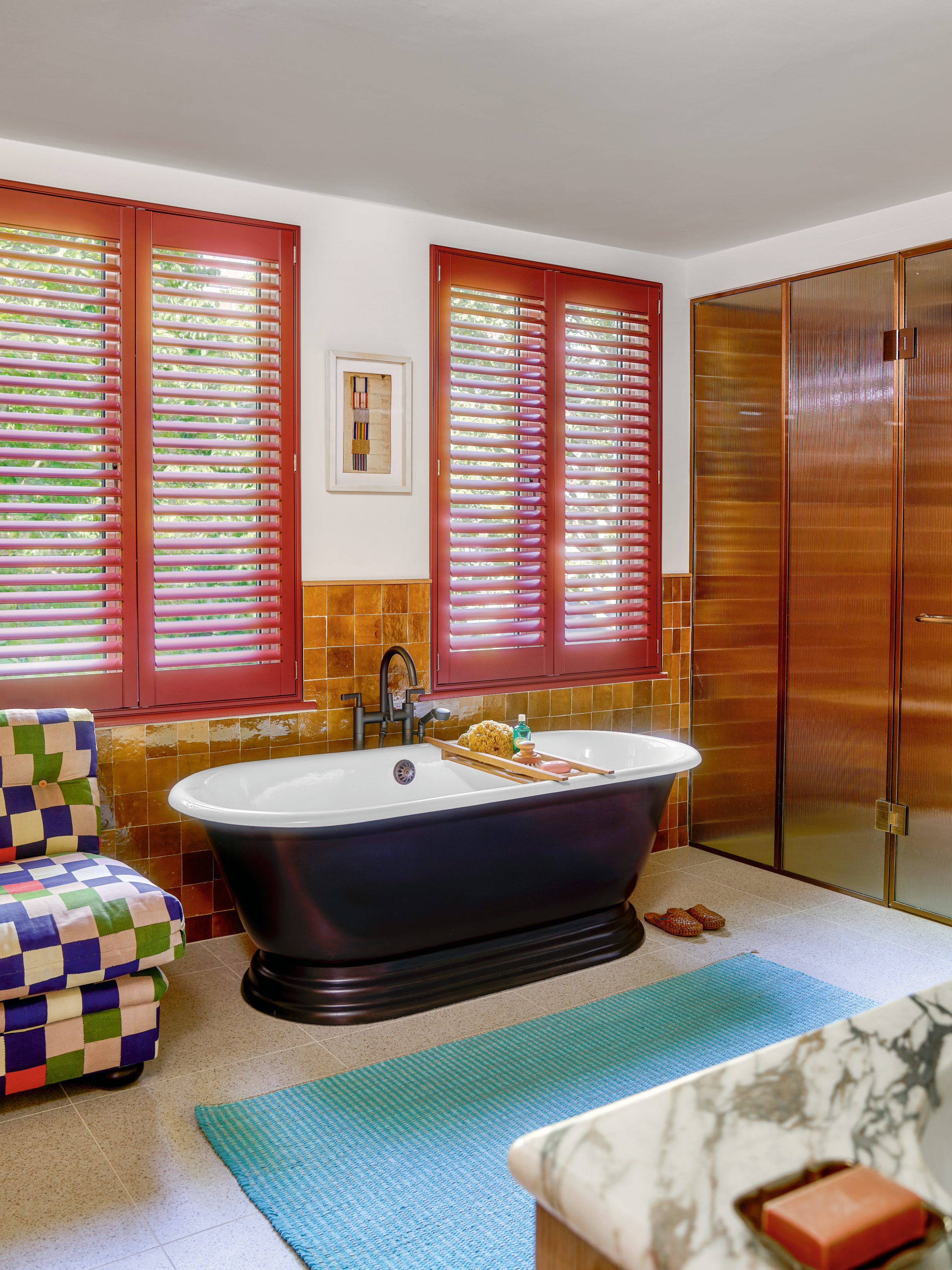 Bathroom with ochre wall tiles, red shutters, black bath and blue rug