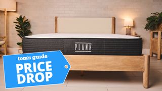 A front on image of the Plank Firm mattress on a bed frame in a bedroom, a Tom's Guide price drop deals graphic in the bottom left corner