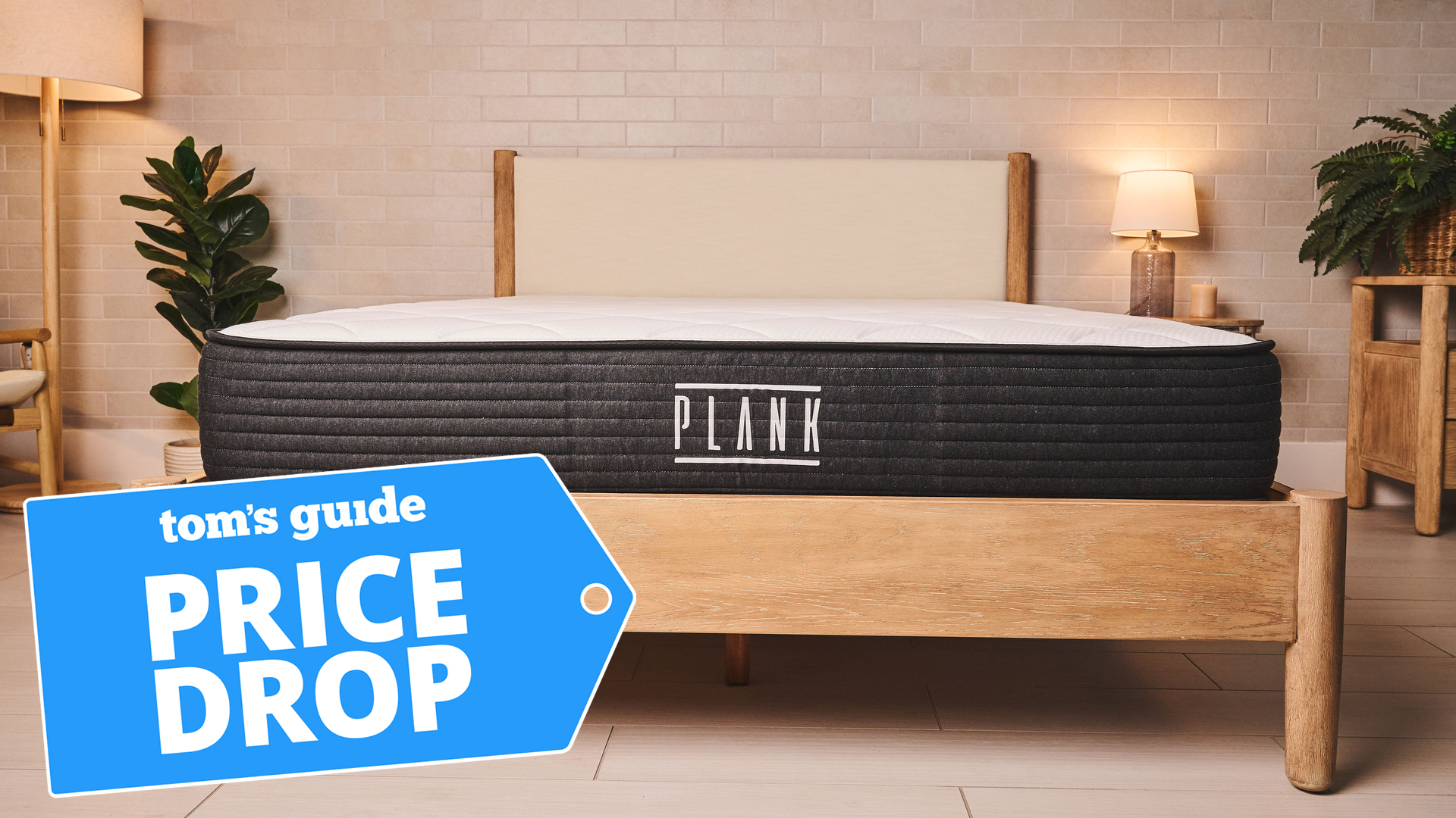 A front on image of the Plank Firm mattress on a bed frame in a bedroom, a Tom's Guide price drop deals graphic in the bottom left corner