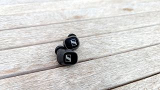 The Sennheiser CX Plus wireless earbuds resting on a wood surface