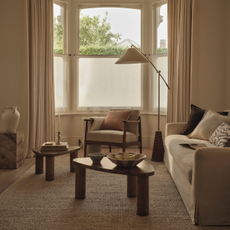 Neutral livging room with two wood coffee table, cream sofa, cream chair and large floor lamp.