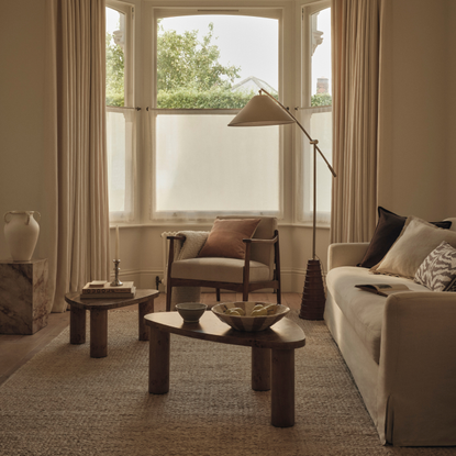 Neutral livging room with two wood coffee table, cream sofa, cream chair and large floor lamp.