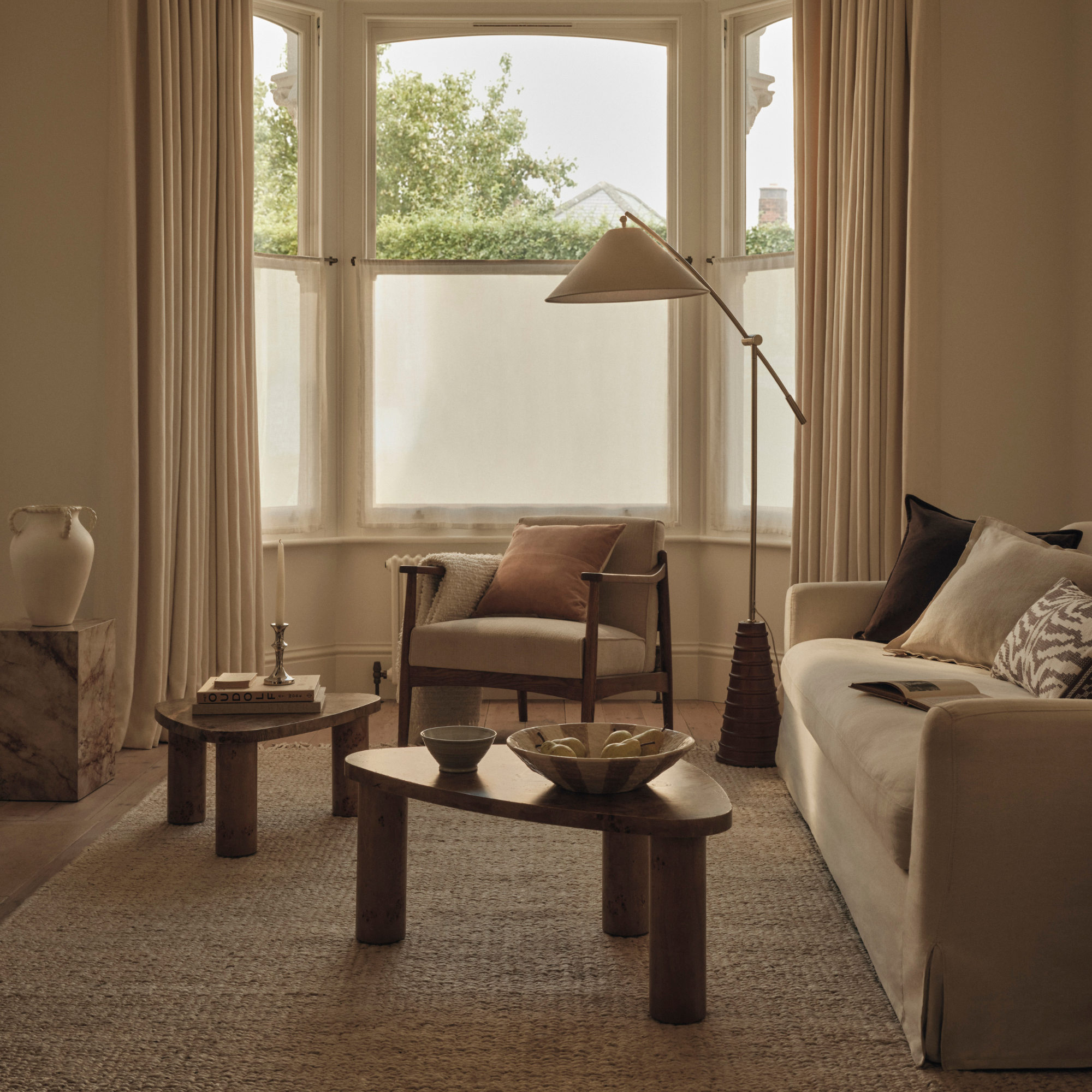 Neutral livging room with two wood coffee table, cream sofa, cream chair and large floor lamp.