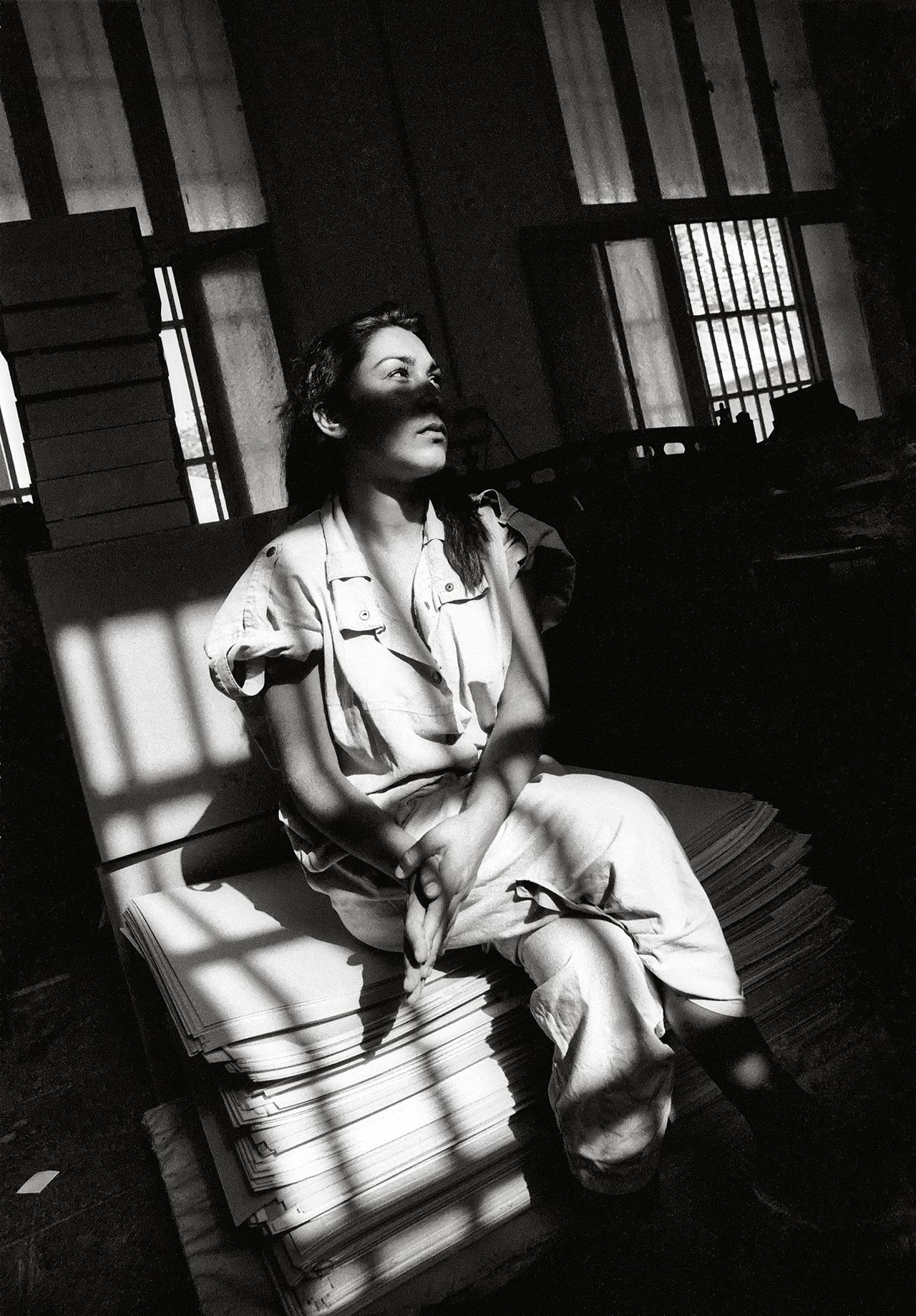 Black and white photograph of a woman sat on a prison bed staring into the distance