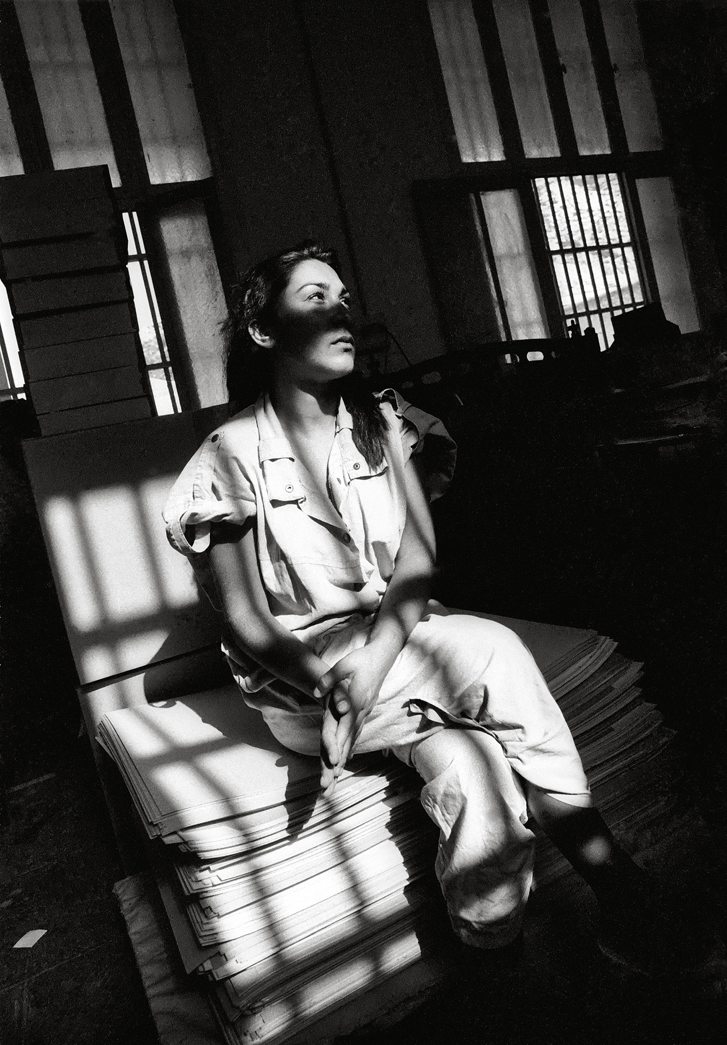 Black and white photograph of a woman sat on a prison bed staring into the distance