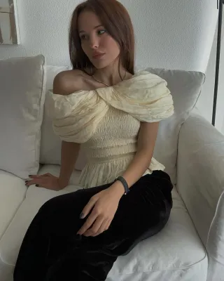 @deborabrosa wearing a pale yellow ruched top with black trousers sitting on couch