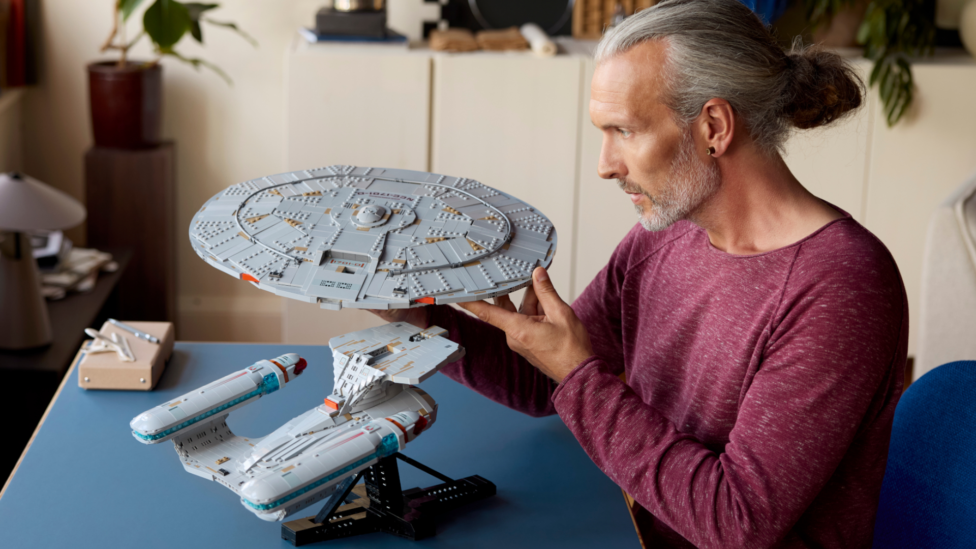 A man detaches the saucer section of the Lego Enterprise while sat at a table