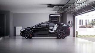 Black Tesla Model Y sitting in a white garage next to a home charger