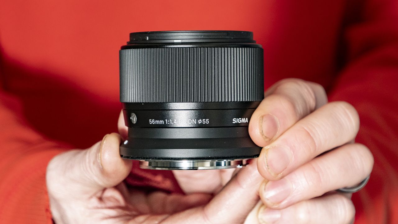 Sigma 56mm F1.4 DC DN Contemporary lens in the hand, orange t-shirt background
